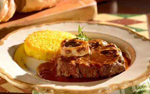 Un succulento ossobuco alla milanese, cotto lentamente e servito con polenta gialla e un rametto di rosmarino.