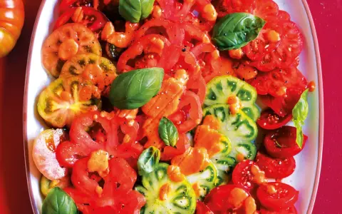 Un colorato carpaccio di pomodoro, con fette di diverse varietà, condito con olio e basilico fresco.