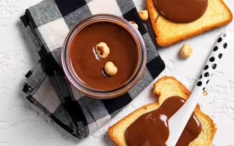 Crema di nocciole fatta in casa in un barattolo, con fette biscottate e nocciole sparse.