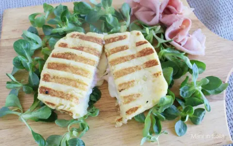 Toast di patate grigliato, ripieno di prosciutto e formaggio filante, servito su un letto di insalata fresca.