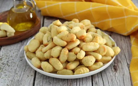 Gnocchi dorati e croccanti, cotti nella friggitrice ad aria, conditi con erbe aromatiche. Accanto, olio d'oliva e gnocchi crudi.