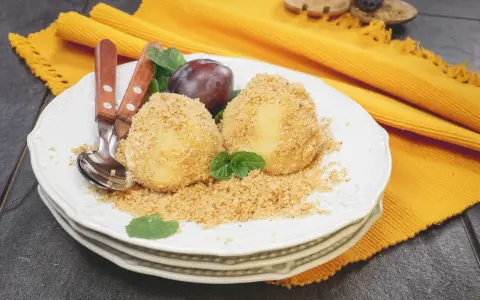 Due deliziosi gnocchi di susine, ricoperti di pangrattato e guarniti con menta, su un piatto bianco con posate.