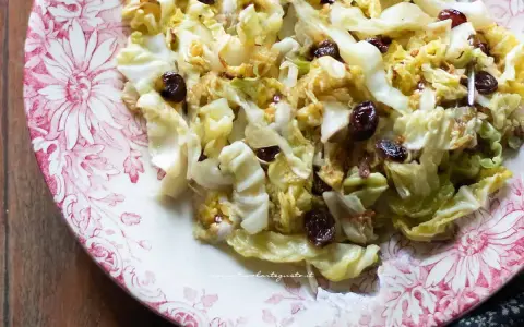 Deliziosa insalata di verza con uvetta, servita su un piatto decorato con fiori rossi.