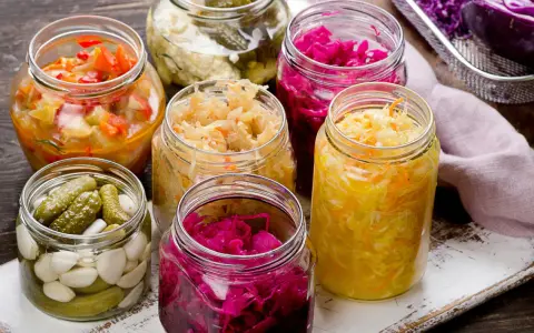Vasi di vetro pieni di cibi fermentati fatti in casa: crauti, cavolo rosso, cetriolini e verdure miste.