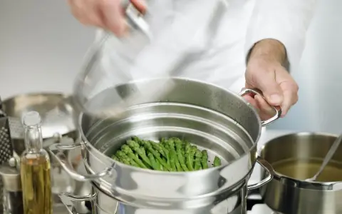 Asparagi freschi pronti per la cottura al vapore in una vaporiera. Un cuoco sta per coprire il cestello.