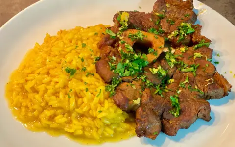Un piatto invitante di risotto giallo cremoso accanto a un ossobuco tenero, guarnito con prezzemolo fresco e scorza di limone.