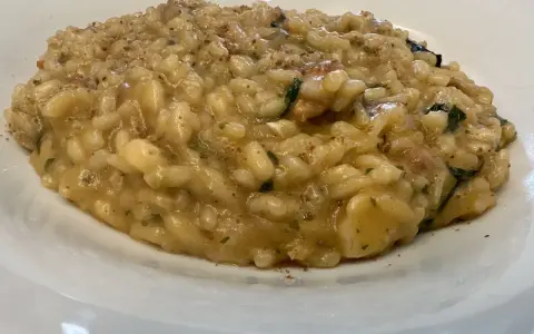 Un cremoso risotto alla pescatora ricetta napoletana, con riso carnaroli e profumi di mare, servito in un piatto bianco.