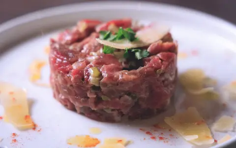 Tartare di manzo, un piatto raffinato. Scopri come condirla per un sapore indimenticabile, con scaglie di parmigiano e un tocco di paprika.