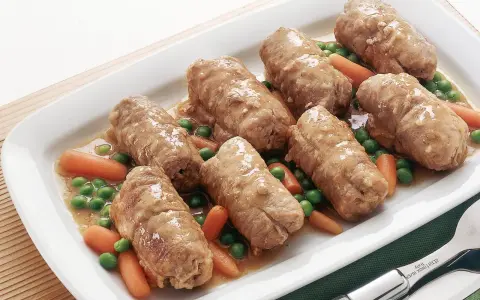 Involtini di carne succulenti serviti con carote e piselli in un piatto bianco.