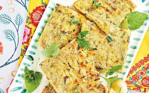 Fette dorate di polpettone di fagiolini, guarnite con erbe aromatiche fresche, su un piatto decorato con motivi floreali vivaci.
