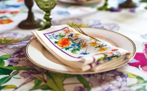 Tovagliolo fiorito piegato su un piatto bianco, con un bordo dorato. La tovaglia è decorata con un motivo floreale vivace. Il tovagliolo va a destra o sinistra?