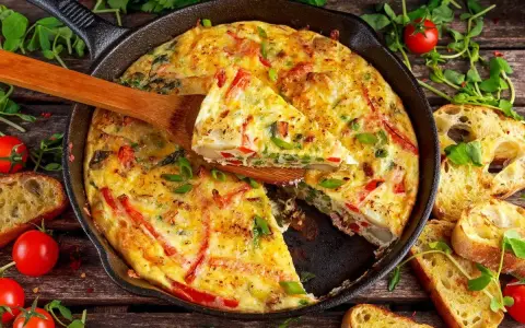 Frittata di peperoni dorata in padella, con fette di pane tostato e pomodorini freschi.