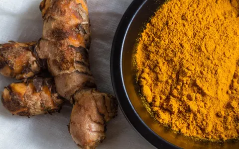 Radici di curcuma e polvere dorata in una ciotola, perfette per dare colore e sapore alla pasta.