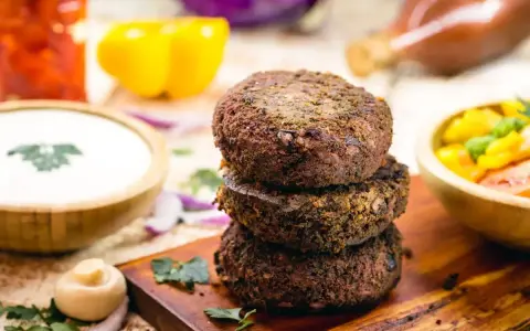 Tre gustosi hamburger di fagioli impilati su un tagliere di legno, con contorni colorati come salsa, peperoni e insalata.