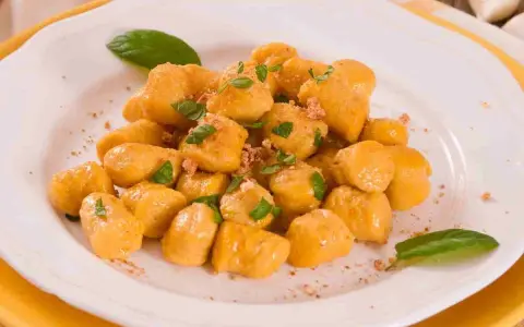 Gnocchi di zucca dorati e soffici, guarniti con basilico fresco e una spolverata di pangrattato croccante, serviti su un piatto bianco.