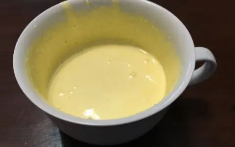 Una tazza bianca contiene un composto giallo pallido, un uovo sbattuto con zucchero, pronto per essere cucinato.