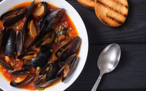 Un invitante piatto di zuppa di cozze in salsa rossa, accompagnato da crostini tostati e un cucchiaio d'argento.