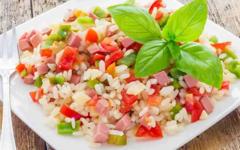 Un colorato insalata di riso con cubetti di prosciutto, peperoni e pomodori, guarnita con foglie di basilico fresco.