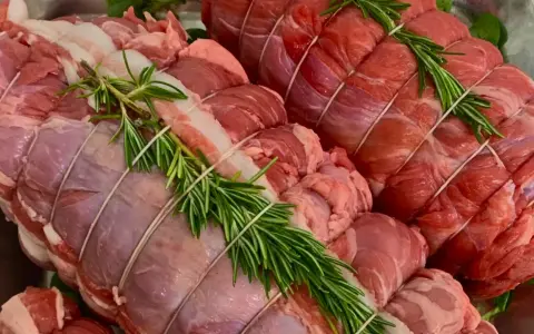 Due **tagli di carne per arrosto** pronti per essere cucinati, legati con spago e guarniti con rametti di rosmarino fresco.