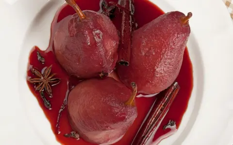 Pere cotte nel vino, profumate con cannella, anice stellato e chiodi di garofano, servite in una ciotola bianca.