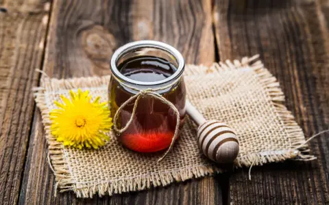 Un vasetto di miele ambrato, un fiore giallo e un cucchiaio di legno su tela grezza. La differenza tra miele e melata è un mistero da svelare.