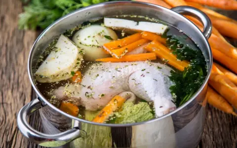 Brodo di pollo in pentola a pressione con carote, cipolla, sedano e prezzemolo.