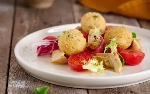 Sfere dorate di miglio fritte, servite con un'insalata fresca di pomodorini, radicchio e pollo. Un'idea gustosa per le tue ricette con miglio.