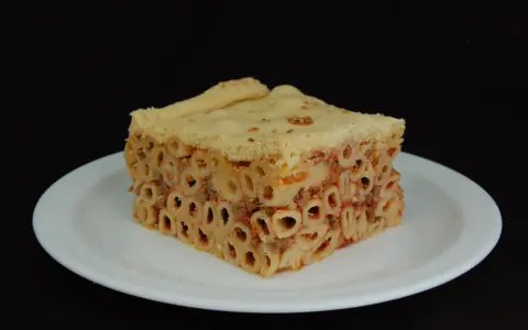Un pezzo di timballo di pasta con ragù e pasta cotta al forno, servito su un piatto bianco.