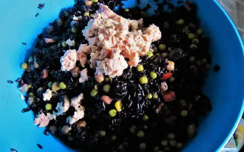 Un'insalata di riso nero con tonno, piselli e cubetti di pomodoro. La cottura del riso nero è perfetta, ogni chicco è ben separato.