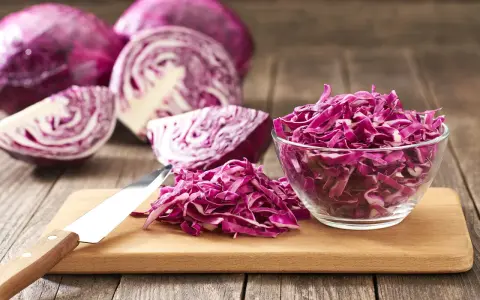 Cavolo cappuccio rosso affettato in una ciotola di vetro e su un tagliere, con cavoli interi e tagliati a spicchi sullo sfondo.