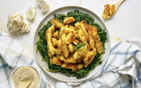 Luganega al forno croccante su letto di verdure verdi. Accanto, aglio e pangrattato.
