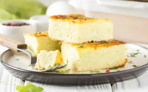 Fetta di frittata al forno soffice e alta, guarnita con erbe aromatiche, su un piatto scuro.