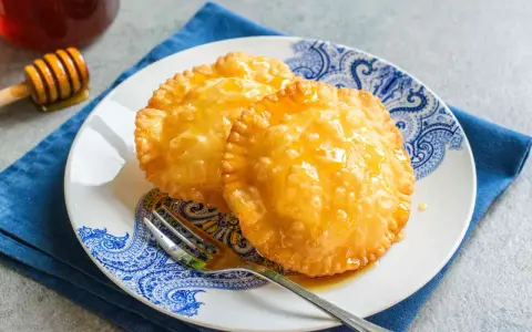 Due dolci sardi fritti, dorati e lucidi di miele, su un piatto blu e bianco con una forchetta.