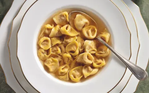 Un primo piatto fumante: tortellini in brodo, un classico della tradizione culinaria italiana, serviti in una ciotola bianca con bordo dorato.
