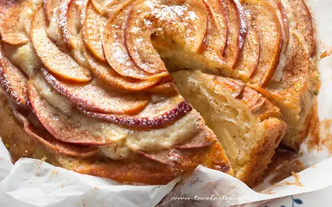 Una fetta di torta di mele e yogurt soffice, con mele a spirale e spolverata di cannella.