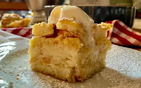 Una fetta di torta di pane raffermo mele e uvetta, cosparsa di zucchero a velo e sormontata da una pallina di gelato.