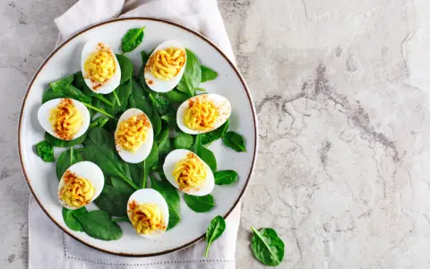 Uova sode ricette sfiziose: uova ripiene su letto di spinaci, guarnite con paprika.