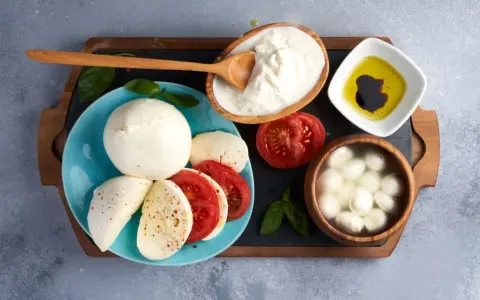 La differenza tra burrata e mozzarella è evidente: la burrata cremosa in ciotola, la mozzarella fresca su piatto con pomodoro.