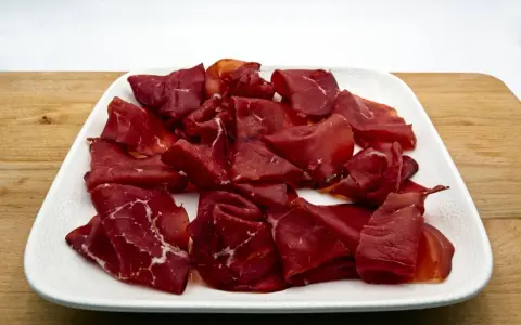 Fette di bresaola, la bresaola che carne è, su un piatto bianco.