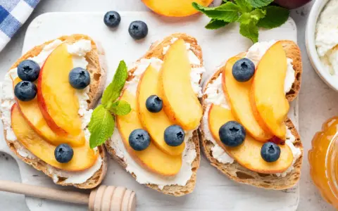 Bruschette con pesche mature, ricotta e mirtilli. Un'idea fresca per ricette con pesche mature, perfetta per la colazione o uno spuntino leggero.