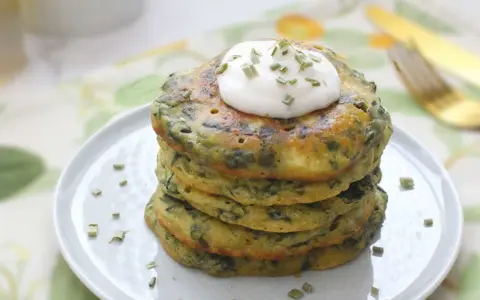 Pancakes salati con farina di grano saraceno e spinaci, guarniti con panna acida e erba cipollina. Un'idea gustosa per le tue ricette con farina di grano saraceno.