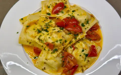 Deliziosi ravioli di pesce conditi con pomodorini e prezzemolo, in un sugo dorato.