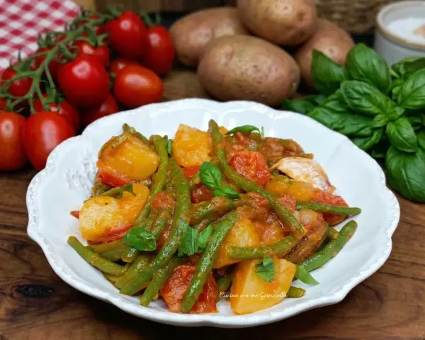 Un piatto di fagiolini e patate alla pugliese, con pomodorini freschi e basilico, pronto per essere gustato.