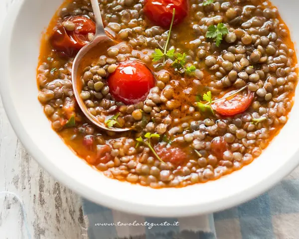 Una ciotola di zuppa di lenticchie veloce con pomodorini e prezzemolo fresco. Un cucchiaio serve la gustosa zuppa.
