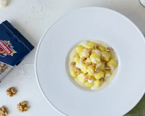 Gnocchi al Castelmagno con noci croccanti, un piatto cremoso e saporito. La confezione di noci Ventura accanto promette un tocco di gusto in più.