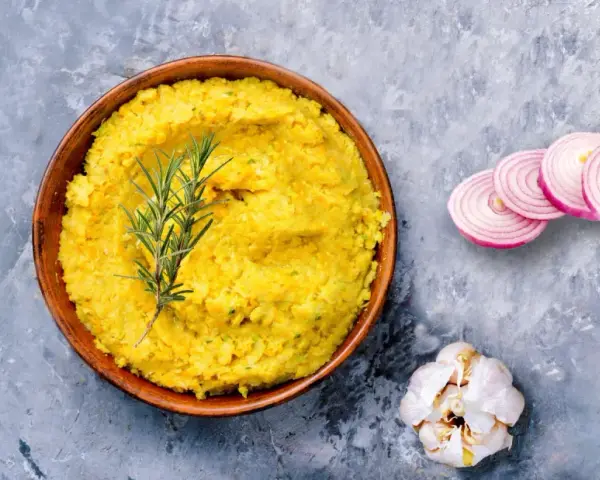 Piatto di lenticchie decorticate cremose, guarnito con rosmarino, cipolla rossa affettata e aglio.