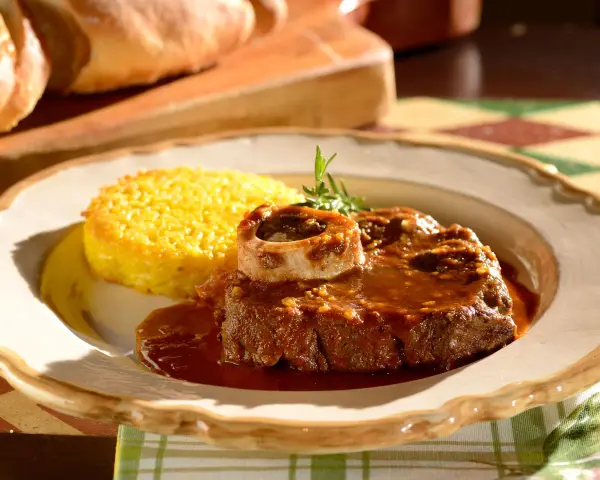 Un succulento ossobuco alla milanese, cotto lentamente e servito con polenta gialla e un rametto di rosmarino.