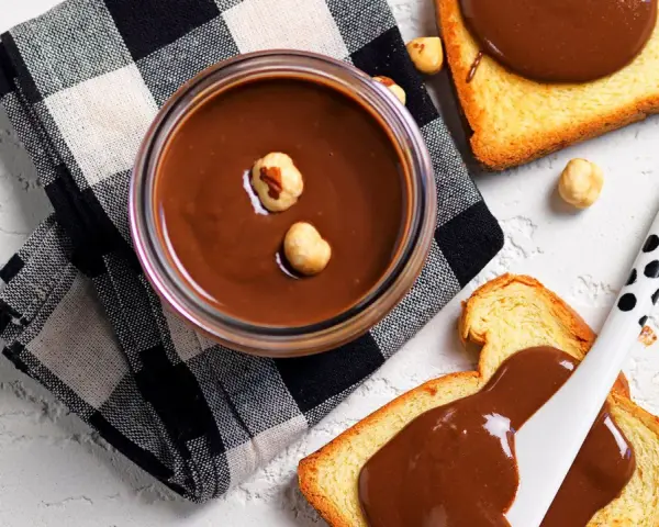 Crema di nocciole fatta in casa in un barattolo, con fette biscottate e nocciole sparse.