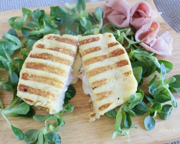 Toast di patate grigliato, ripieno di prosciutto e formaggio filante, servito su un letto di insalata fresca.