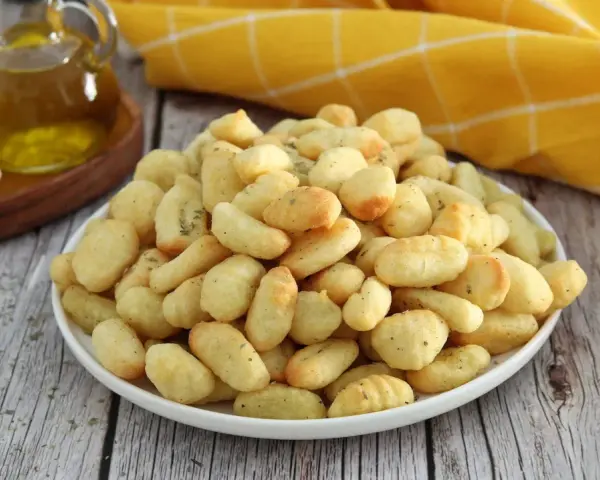 Gnocchi dorati e croccanti, cotti nella friggitrice ad aria, conditi con erbe aromatiche. Accanto, olio d'oliva e gnocchi crudi.